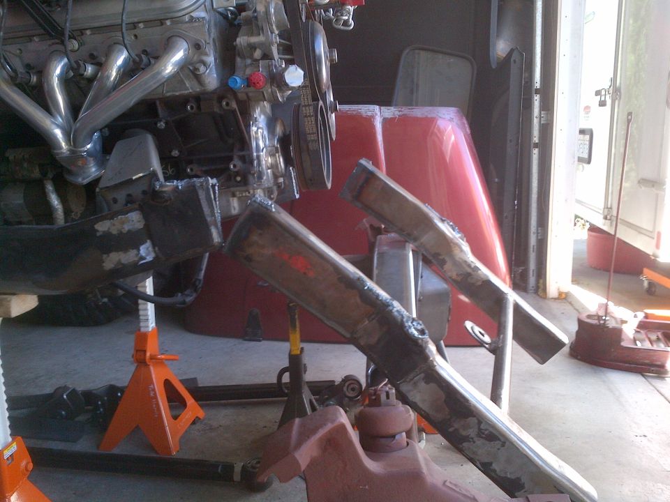 Engine and exhaust headers mounted on jack stands with frame components visible