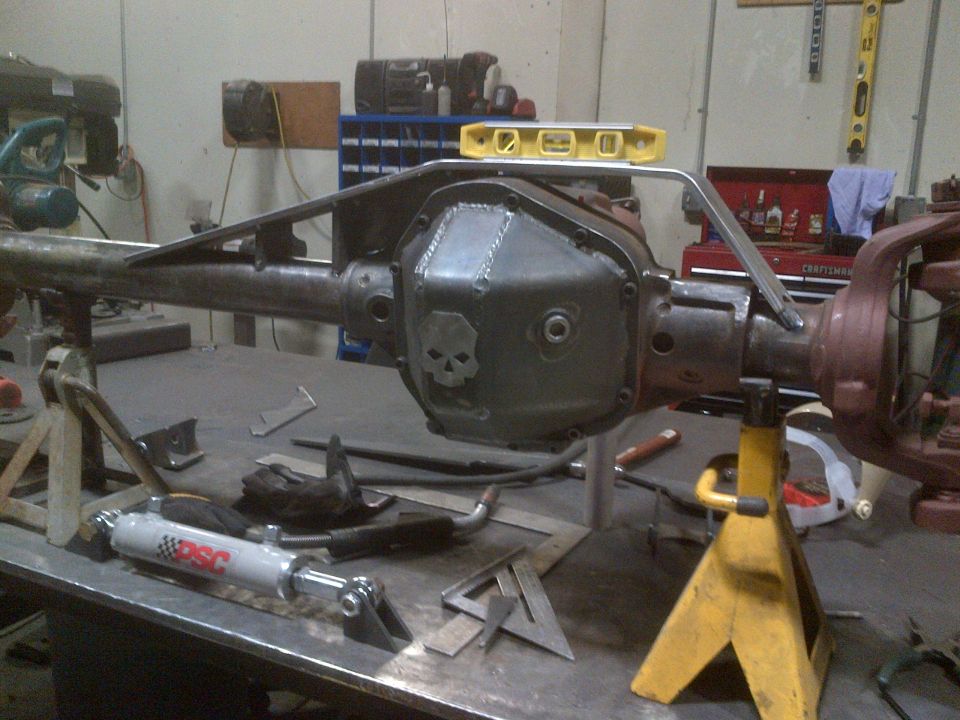 Differential housing with custom skull cover, supported by jack stands, with a steering stabilizer and tools on a workbench