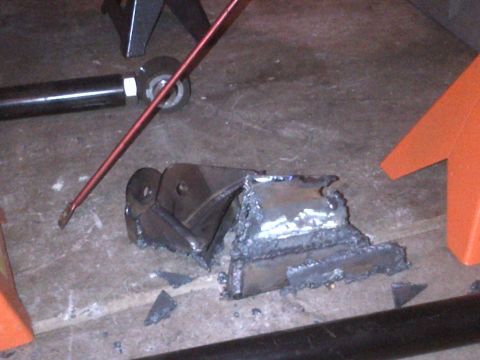 1985 Jeep CJ7 - A damaged metal bracket lies on a concrete surface, with a red rod and part of an orange jack stand visible.