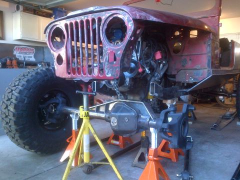 1985 Jeep CJ7 - This Jeep CJ-series front end is undergoing work, with the engine exposed and the vehicle supported by jack stands.