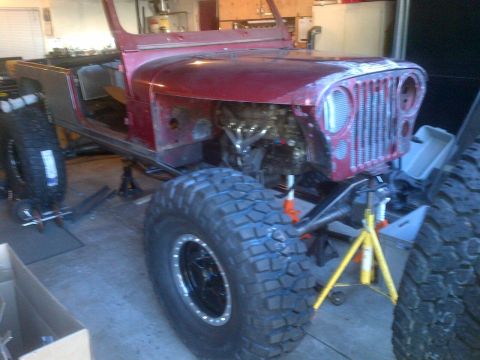 1985 Jeep CJ7 - This red Jeep CJ-series body is undergoing modifications, with its engine exposed and large off-road tires fitted.