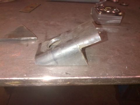 1985 Jeep CJ7 - A metal bracket with a hole and angled cut sits on a workbench next to other metal pieces.