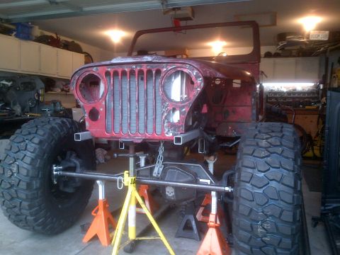 1985 Jeep CJ7 - This Jeep CJ-series is in a garage, elevated on jack stands with massive tires, suggesting a custom build or repair.
