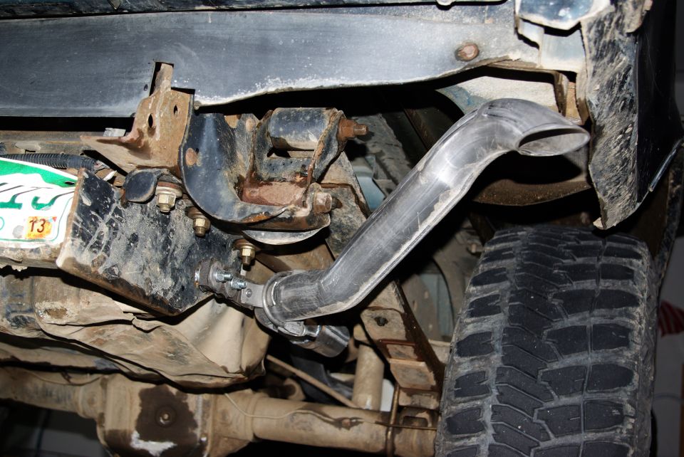Close-up of a custom exhaust pipe attached to a vehicle's undercarriage, near the rear tire