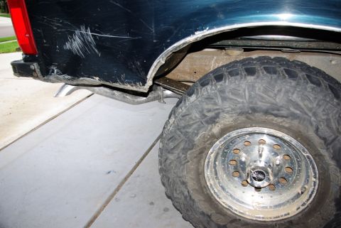 1995 Ford Bronco - A dark blue vehicle's rear quarter panel shows significant damage and rust near the wheel well.