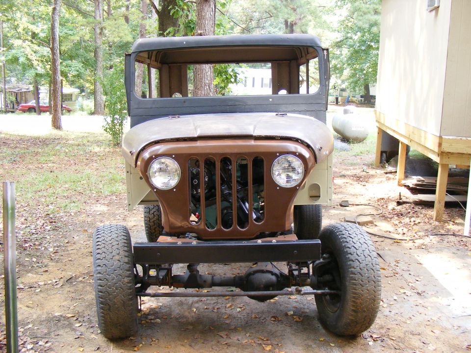 Jeep CJ-5 front end with brown grille and tan fenders, large tires, and exposed engine components