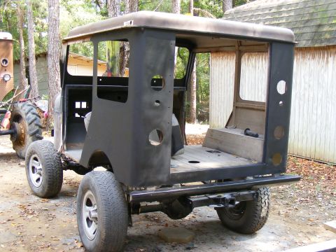 Rear view of a dark-colored, partially restored off-road vehicle with a hardtop