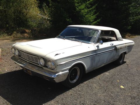 1964 Ford Fairlane - A white 1964 Ford Fairlane coupe sits on a gravel surface, showing primer patches on its bodywork.