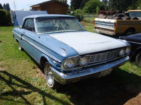 1964 Ford Fairlane - A classic coupe sits in a grassy yard next to a pickup truck, with a shed and trees in the background.