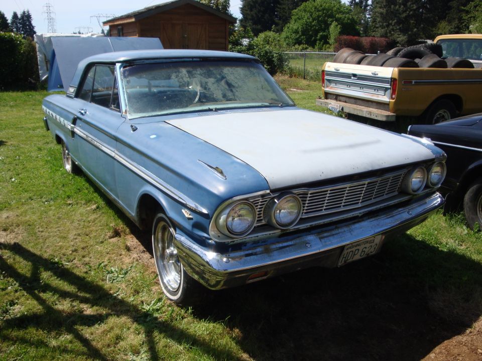 Blue and white coupe with a gray hood. License plate reads HDP 623. A yellow pickup truck is parked behind it