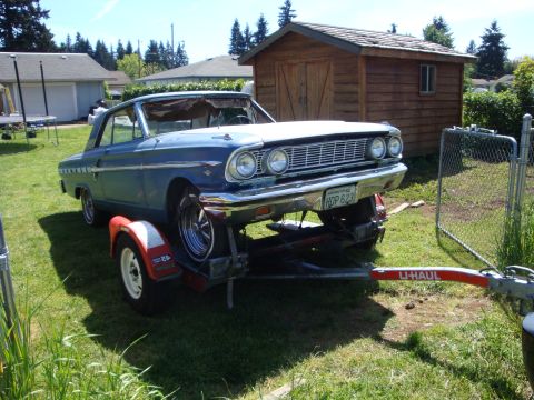 1964 Ford Fairlane - A blue 1964 Ford Fairlane is loaded onto a U-Haul trailer, parked in a residential backyard.
