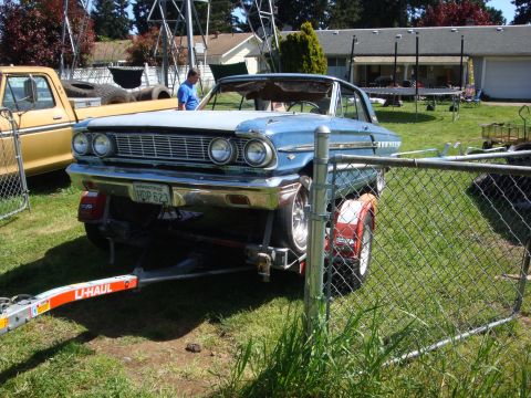 1964 Ford Fairlane - A blue 1964 Ford Fairlane is loaded onto a U-Haul trailer, parked next to a yellow pickup truck.