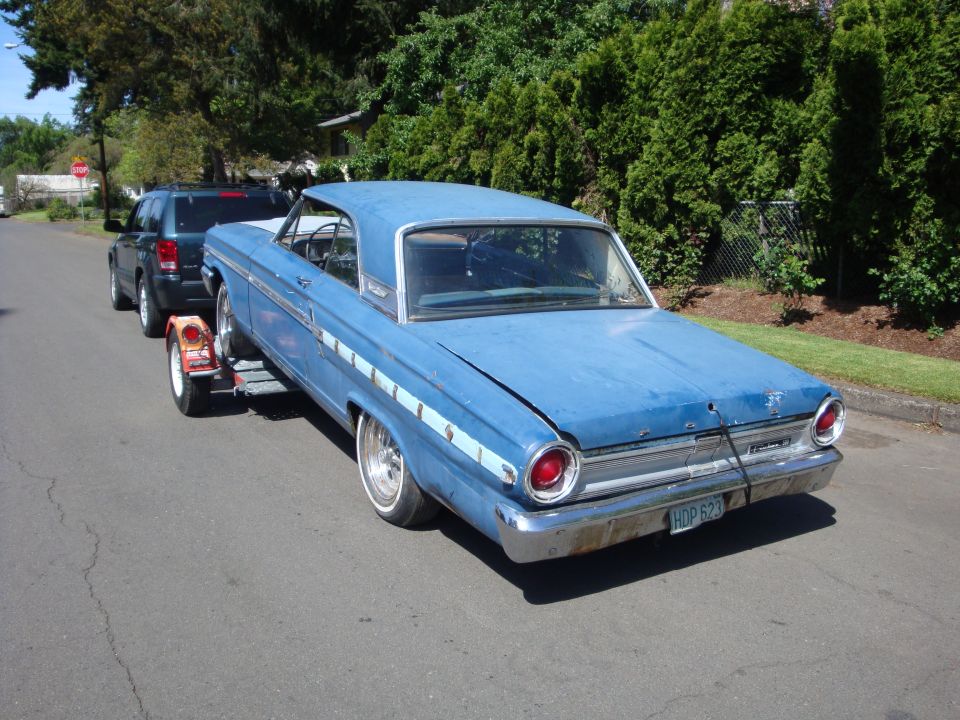 Blue 1964 Ford Fairlane coupe being towed on a trailer, rear view