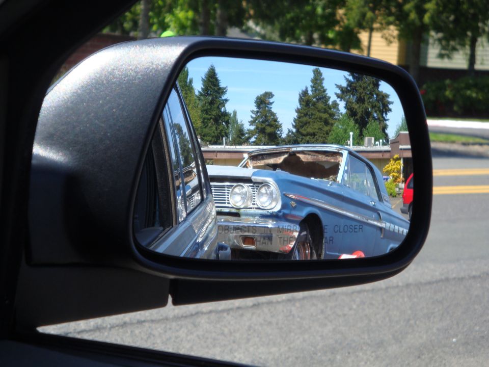 Side mirror view of a blue 1962 Chevrolet Impala with a damaged roof