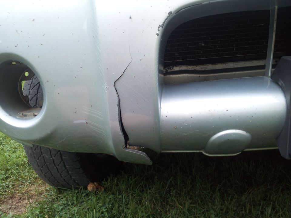 Silver truck bumper with a large crack, showing a tire and grass