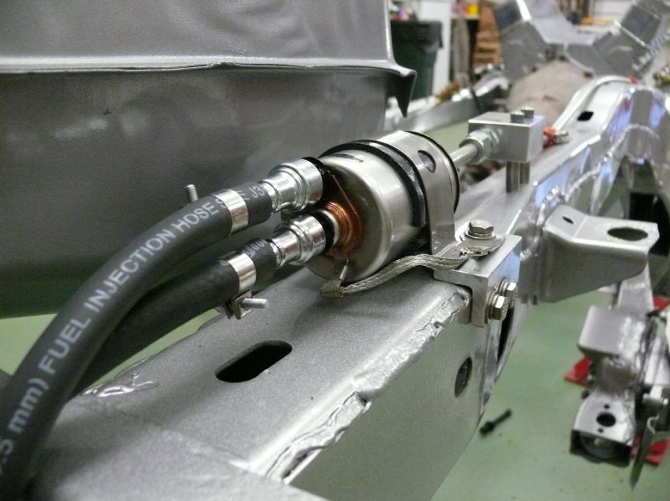 Fuel filter with "FUEL INJECTION HOSE" printed on hoses, attached to a bare metal vehicle frame
