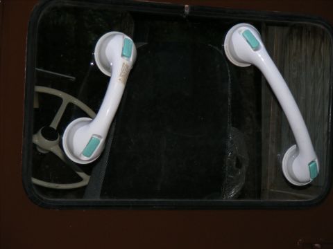 Two white suction cup grab bars attached to the inside of a vehicle window. A steering wheel is visible throug