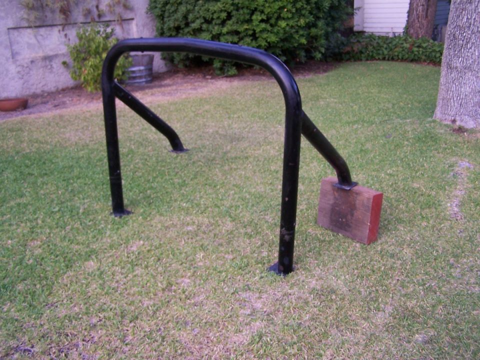 Black metal frame on grass, supported by a wooden block.