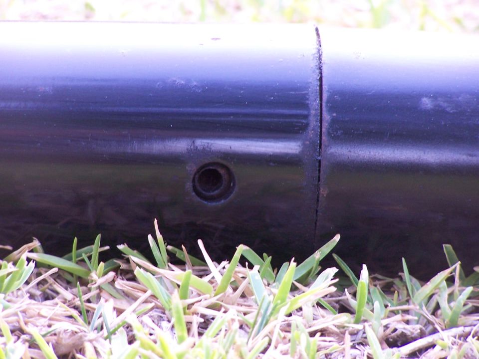 Black metal pipe with a hole and seam, resting on grass