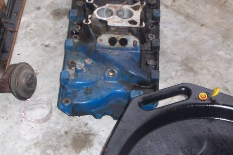 1980 Ford Bronco - A blue engine intake manifold is shown on a concrete floor next to an oil drain pan.