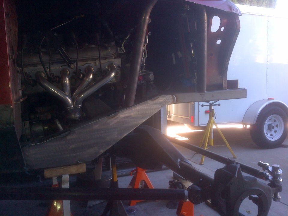 Custom vehicle chassis with engine and headers, supported by jack stands.