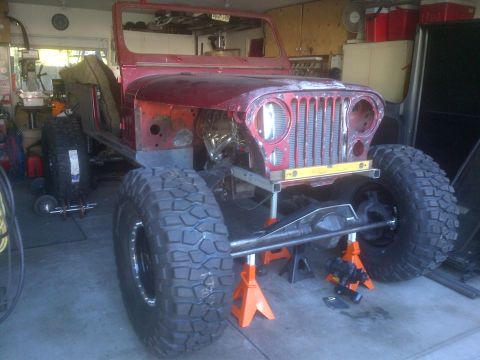 1985 Jeep CJ7 - This Jeep CJ-series is in a garage, lifted on jack stands with its body and large tires visible.