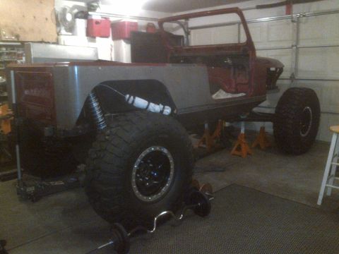 1985 Jeep CJ7 - This Jeep CJ body is undergoing work in a garage, with large tires and suspension components visible.