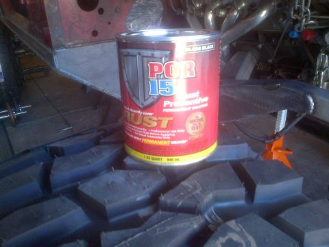 1985 Jeep CJ7 - A can of POR-15 rust preventive paint is placed on a tire, with parts of a vehicle's frame and exhaust system in the background.