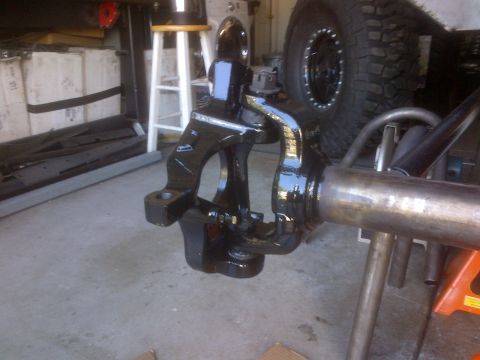 1985 Jeep CJ7 - Close-up of a black painted front axle assembly, likely for an off-road vehicle, with a large tire in the background.