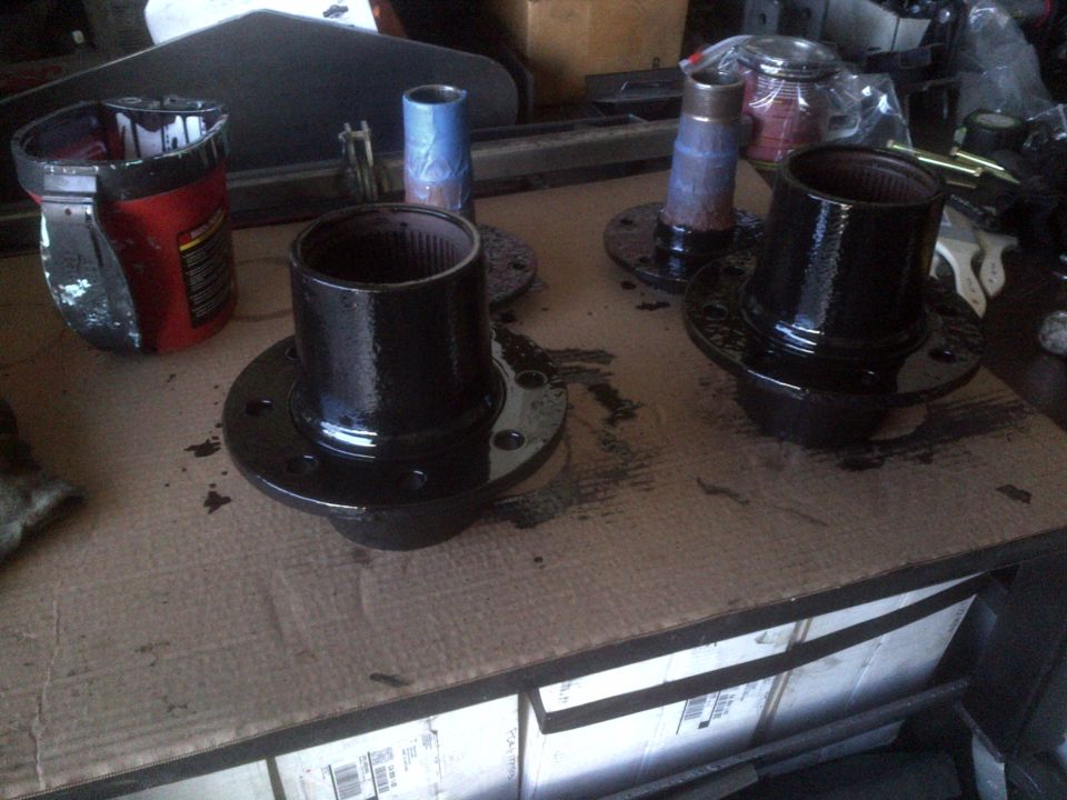 Two black painted automotive hubs with splined bores sit on a cardboard surface next to a red and black can