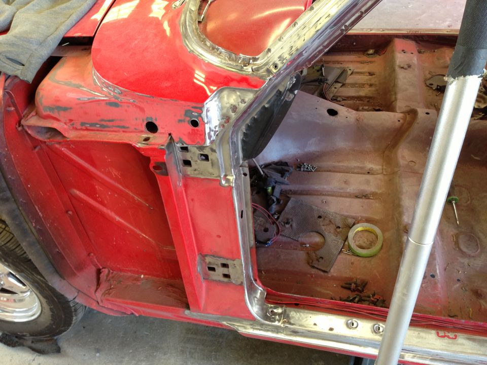 Red car interior with exposed metal, door frame, and floor pan. Tape and tools are visible