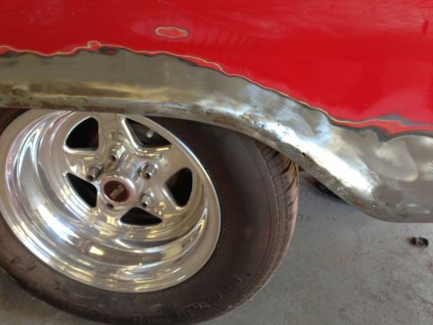 1964 Ford Fairlane - The fender of a red car is being prepped for paint, revealing bare metal and primer around the wheel well.