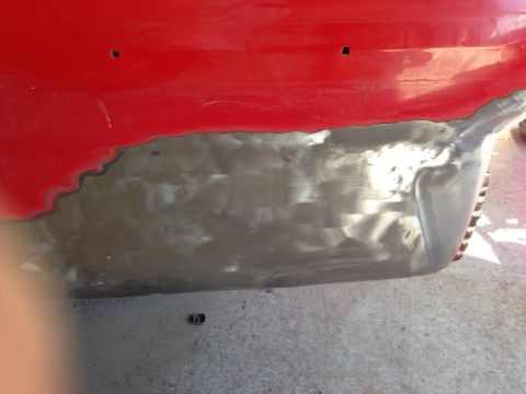 1964 Ford Fairlane - Close-up of a red car's body panel undergoing repair, showing exposed metal and primer.