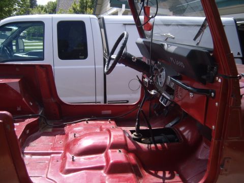 1985 Jeep CJ7 - Interior view of a red Jeep, stripped down for work, with a white truck visible in the background.
