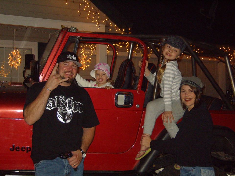 Family posing with a red 1985 Jeep CJ7, decorated with Christmas lights