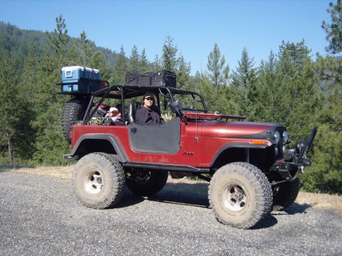 1985 Jeep CJ7 - This red Jeep CJ is equipped for an off-road adventure, carrying gear on its roof rack and spare tire carrier.