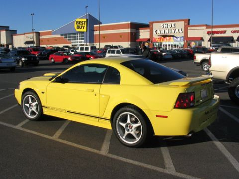 2003 Ford Mustang - A yellow 2003 Ford Mustang is parked in a shopping center lot.