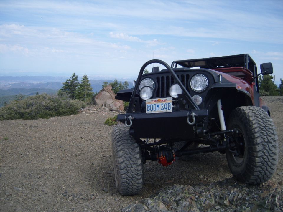 1985 Jeep CJ7 with custom front bumper and off-road tires parked on a rocky overlook