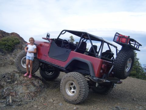 1985 Jeep CJ7 - A girl poses next to a modified red Jeep CJ-series off-road vehicle on a rocky trail.