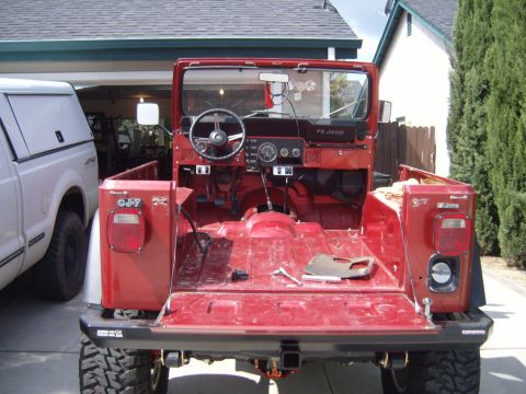 1985 Jeep CJ7 - The interior and rear of a red Jeep CJ-7 are visible, with the tailgate down and a white pickup truck parked alongside.
