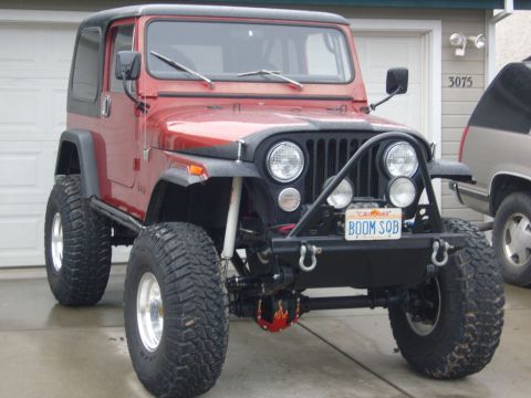 1985 Jeep CJ7 - A red Jeep CJ is parked in front of a garage, with another SUV visible to the right.