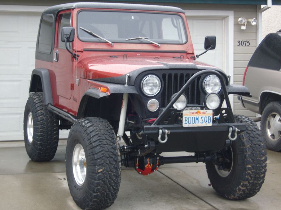 Red Jeep CJ with black hardtop, off-road tires, and custom front bumper. License plate reads BOOM SQB