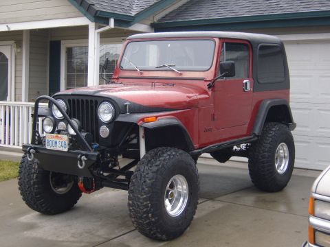 1985 Jeep CJ7 - This red Jeep CJ features a black hardtop, aggressive off-road tires, and a custom front bumper with auxiliary lights.