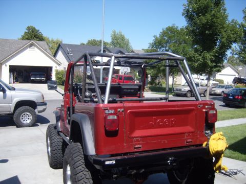 1985 Jeep CJ7 - This red Jeep CJ-7 features a prominent roll cage and a custom rear bumper, with another vehicle visible in the driveway.