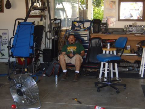 1985 Jeep CJ7 - A man relaxes in a cluttered garage, surrounded by various equipment and tools.