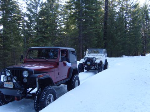 1985 Jeep CJ7 - Two Jeeps, a red CJ7 and a white CJ7, navigate a snow-covered forest road.