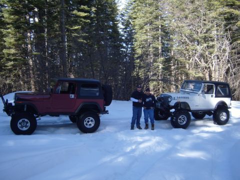 1985 Jeep CJ7 - Two Jeep CJ models are parked in the snow with two people standing between them in a wooded area.