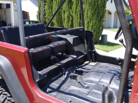 1985 Jeep CJ7 - The interior of a red Jeep CJ shows black seats, a roll cage, and a textured floor.
