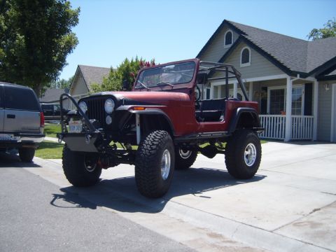 1985 Jeep CJ7 - This red Jeep CJ7, modified for off-road use, is parked in a suburban driveway.