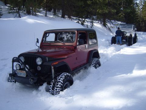 1985 Jeep CJ7 - Two Jeeps navigate a snowy forest road, with the lead Jeep CJ7 partially submerged in snow.
